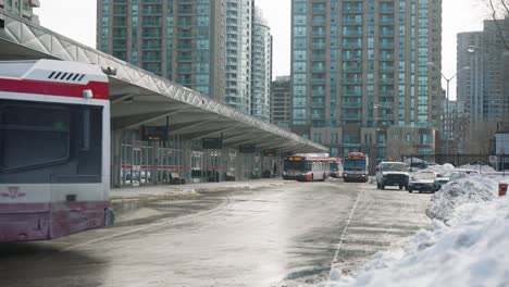 bus driving off from a bus station in winter, buildings in the background. snow banks near by.