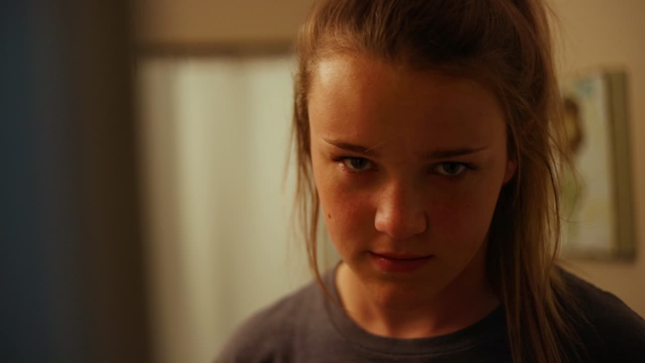 Creepy slow Motion panning shot of a young girl seriously staring at the camera and smiling really evilly right before she falls out of frame