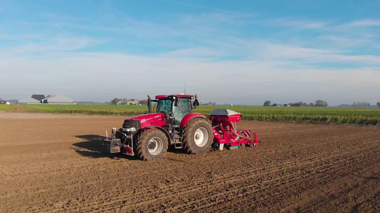 새 그림자가 지나가는 화창한 날에 갈색 흙밭을 갈고 있는 빨간 트랙터