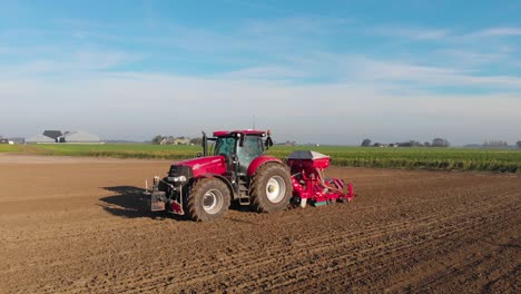 Roter-Traktor,-Der-An-Einem-Sonnigen,-Frischen-Tag-Ein-Braunes,-Erdiges-Feld-Pflügt,-Mit-Vorbeiziehenden-Vogelschatten