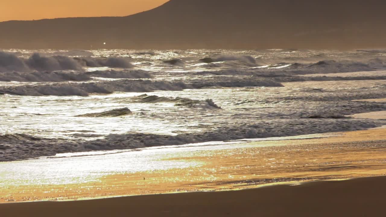 Slow motion waves rolling onto golden sandy beach at dawn