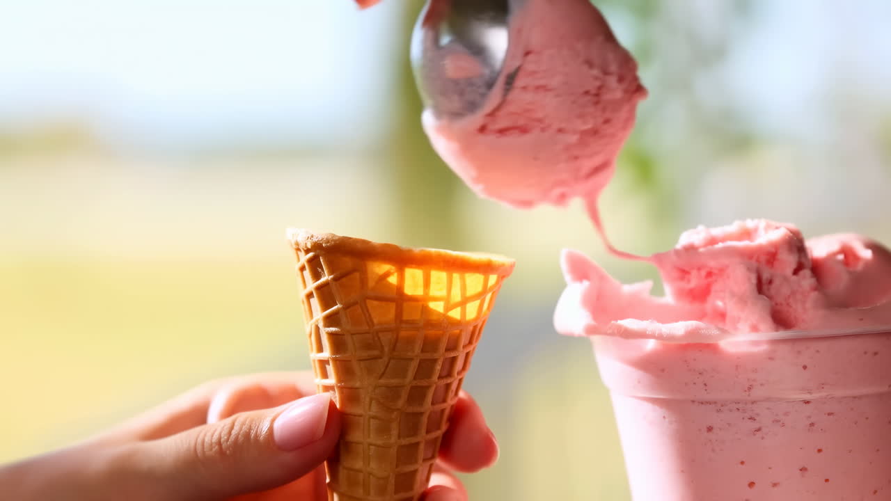 Primer plano de manos sirviendo helado rosa en un cono de barquillo