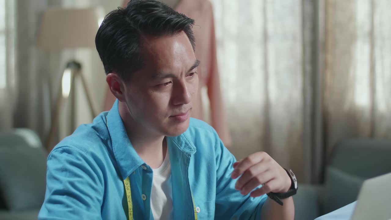 아시안 남성 디자이너가 노트북에서 작업하고 생각하고 스튜디오에서 옷을 디자인하는 동안 지표손가락을 올리고 있습니다.