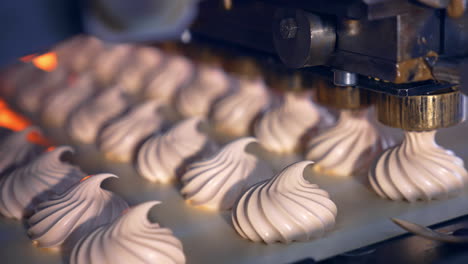 creamy marshmallows being squeezed onto the conveyor belt. well-coordinated work of the molding machine producing tasty sweets. process in close up.