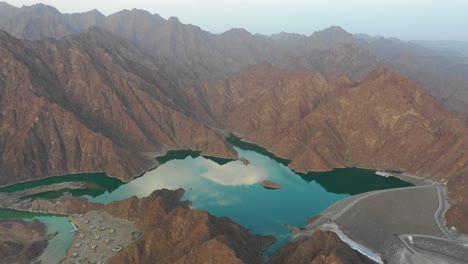 Magical-dreamy-aerial-view-of-a-lake-surrounded-by-endless-mountains-with-clouds-reflection-on-the-water