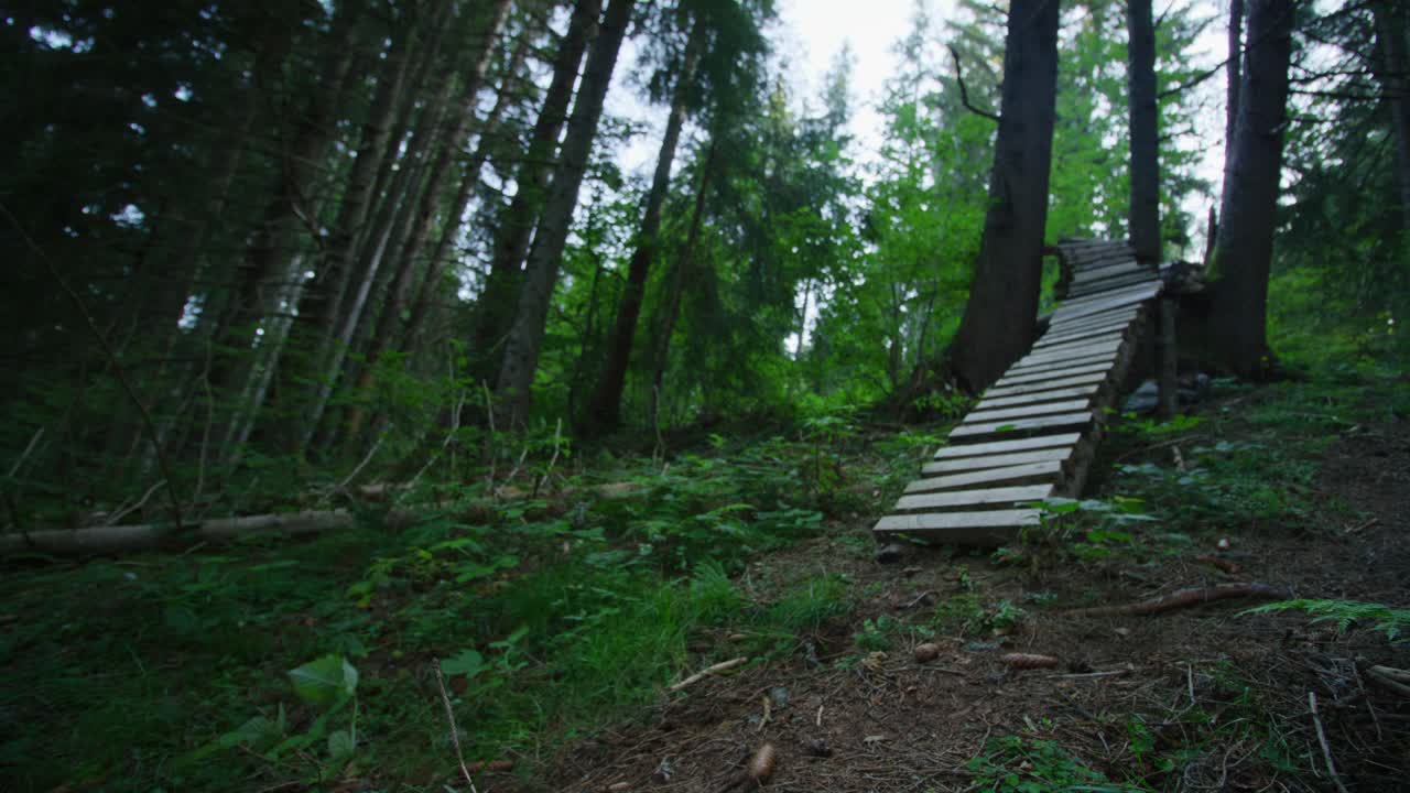 un ciclista de montaña baja por un estrecho puente técnico en el bosque