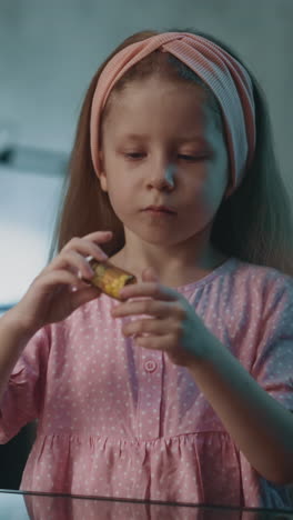 lovely little girl with pink headband takes small bottle with vitamin medicines sitting at glass table in darkened room at home close view slow motion