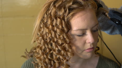 hairdresser curls young redheads hair with curling iron, close up