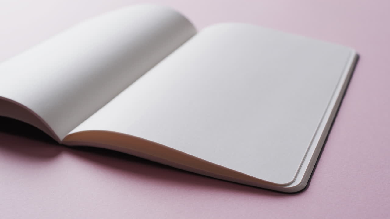 Close up of open blank book with copy space on pink background in slow motion