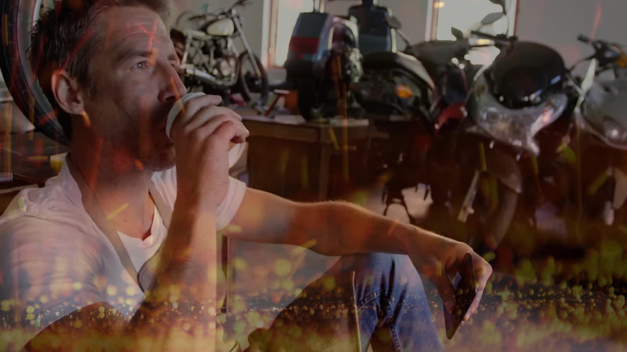 Man sipping coffee while browsing phone in motorcycle workshop, showing animated bokeh lights