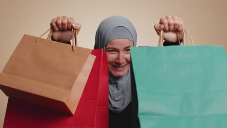 happy muslim woman showing shopping bags, advertising holidays discounts, amazed with low prices