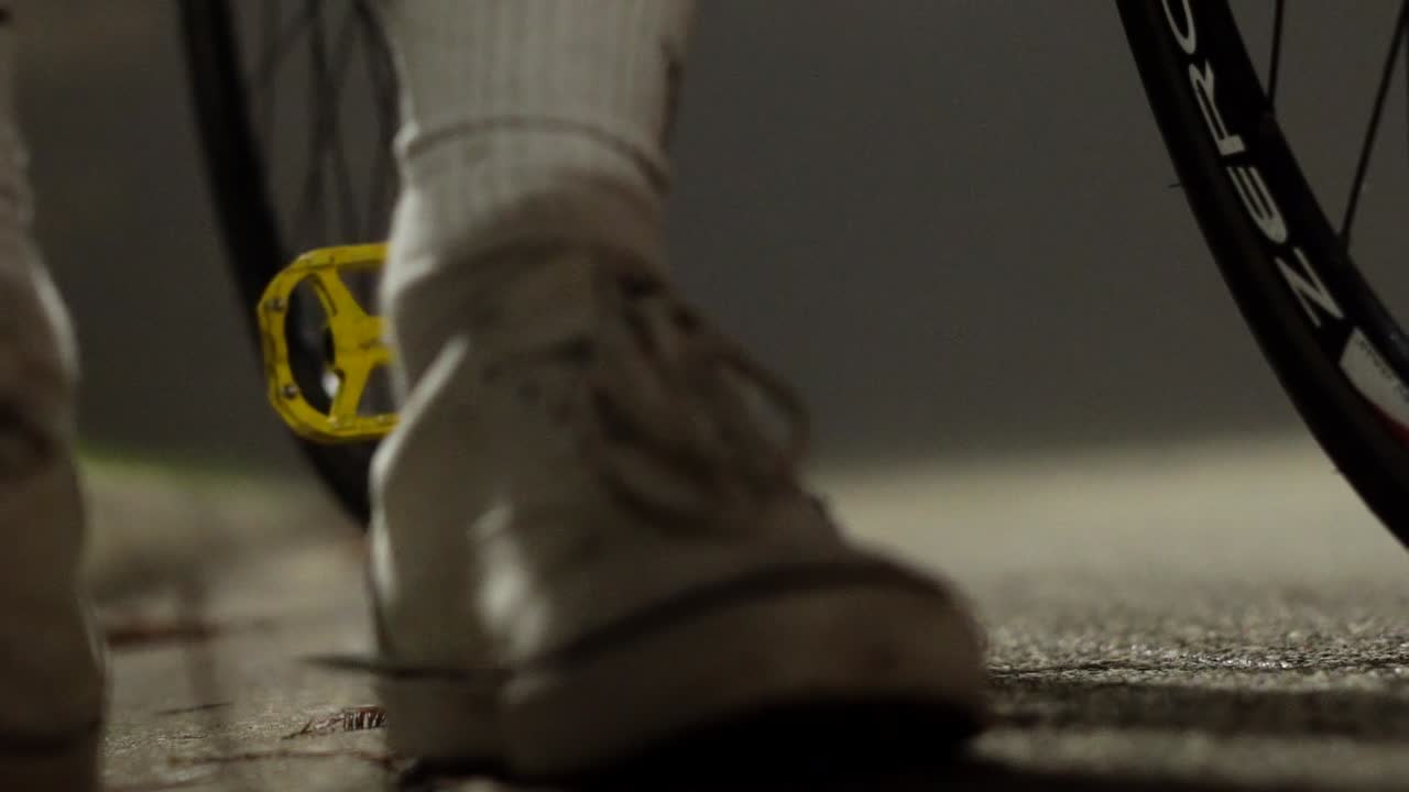 toma cinematográfica de un ciclista bajándose de la bicicleta mientras viaja en un pie en una noche nublada