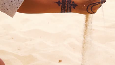 a beautiful woman with henna tattoos picks up sand in her hand in slow motion