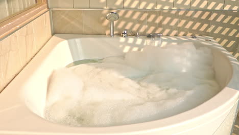 static shot of an empty bath with water flowing from the sink with white foam on the surface