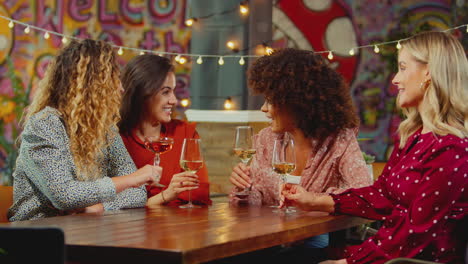 group of multi-cultural female friends sitting at table drinking wine enjoying girls night out