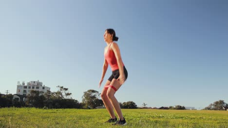 Eurasian-woman-does-squat-jumps-in-the-park-with-booty-band