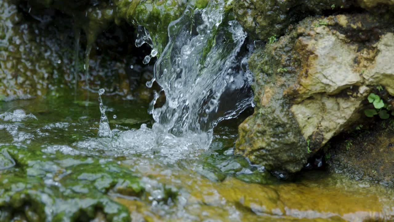 Clear water cascades over moss-covered rocks, creating bubbles and ripples in natural daylight