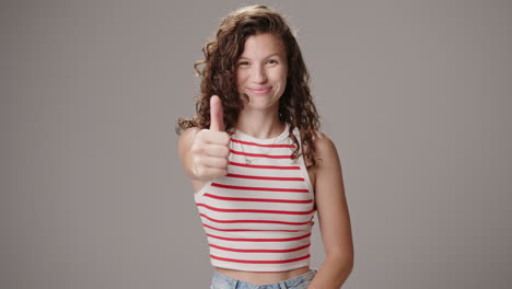 young smiling brunette woman makes thumbs up sign, studio shot