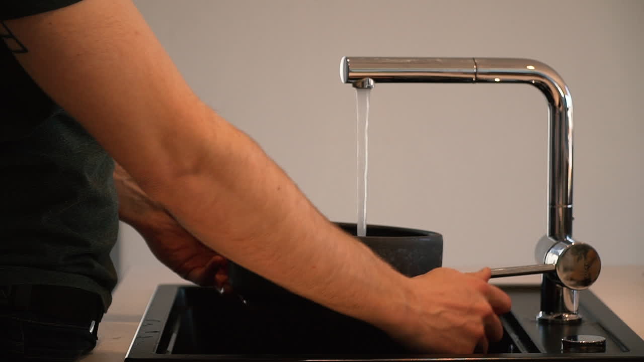 persona llenando un recipiente con agua del grifo en la cocina.