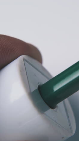 young person puts green color pencil into white plastic sharpener on light background extreme close view