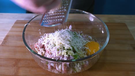 rallar parmesano en la mezcla de albóndigas en un recipiente de vidrio