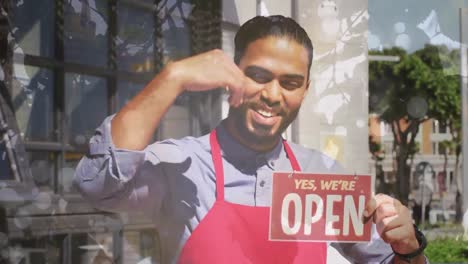 Animation-of-portrait-of-biracial-male-shop-assistant-with-open-sign-over-leaves