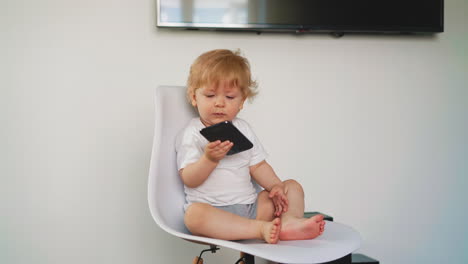 toddler boy in white t-shirt gives mobile phone on chair