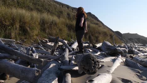 A-man-with-long-red-hair-almost-falls-while-stepping-onto-a-driftwood-trunk