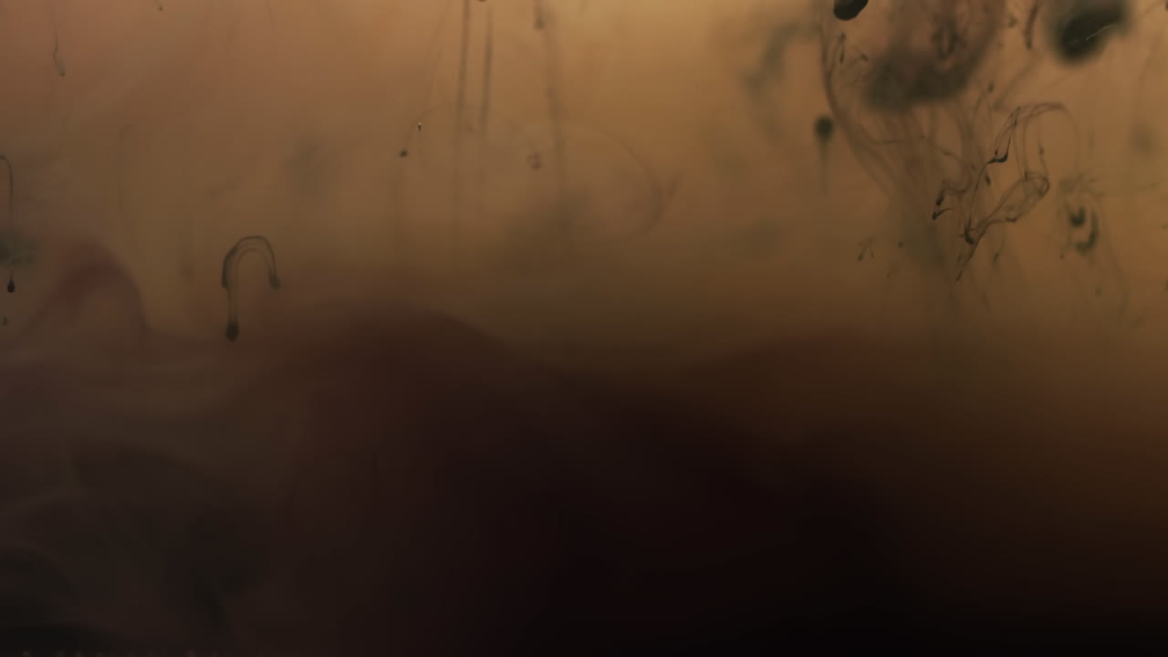 video en cámara lenta de tinta de acuarela negra mezclándose en agua contra un fondo marrón