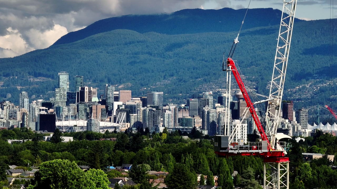 Construction Above Kerrisdale, Backdropped By Downtown Vancouver Skyline, Lush Greenery And Forested Mountains. drone sideways shot