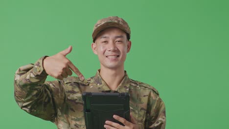 close up of asian man soldier smiling and pointing to a tablet in his hand while standing in the green screen background studio