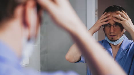 doctor-takes-off-mask-looking-into-large-mirror-in-bathroom