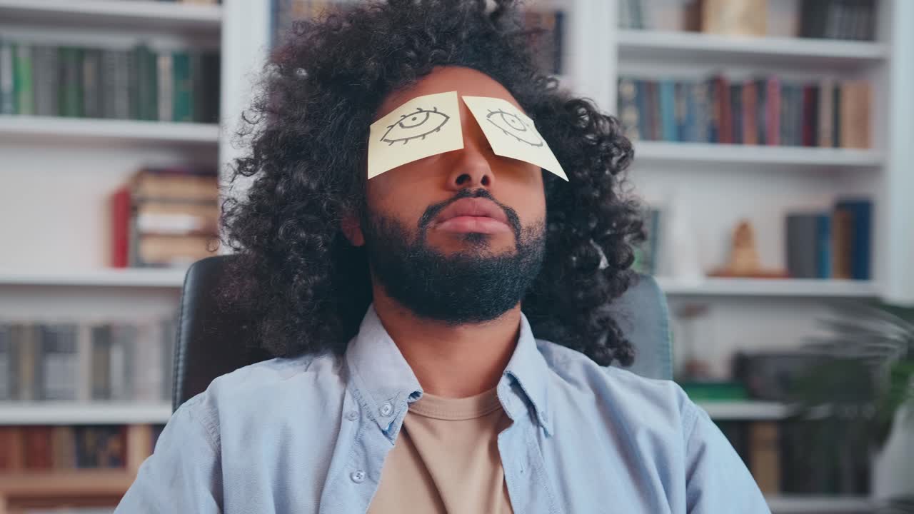Tired young arabian man sleeps working with paper stickers in front of eyes