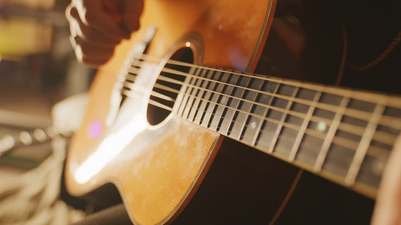 Static close-up of a hand picking guitar strings in a warm, cozy studio