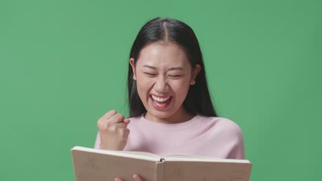 아시아 여학생이 책을 읽고 그린 스크린 스튜디오에서 축하하고 있습니다.