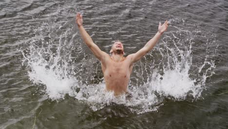 Caucasian-man-having-a-good-time-on-a-trip-to-the-mountains,-wearing-swimming-trunks-and-swimming-an