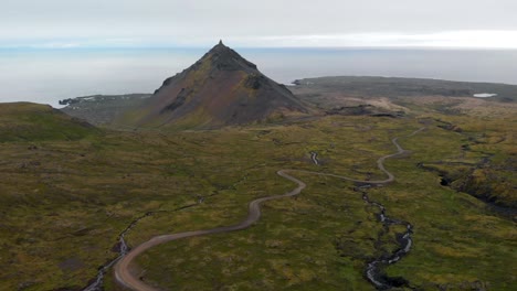 Aerial, drone shot over icelandic wilderness, towards a hill and the sea, on a dark, overcast day, in Snaefellsnes peninsula, in western Iceland