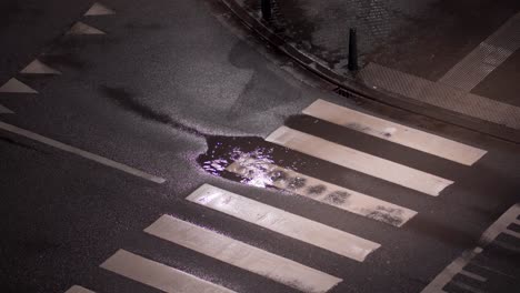 heavy rainfall forms a puddle of water on the crosswalk in the street at night