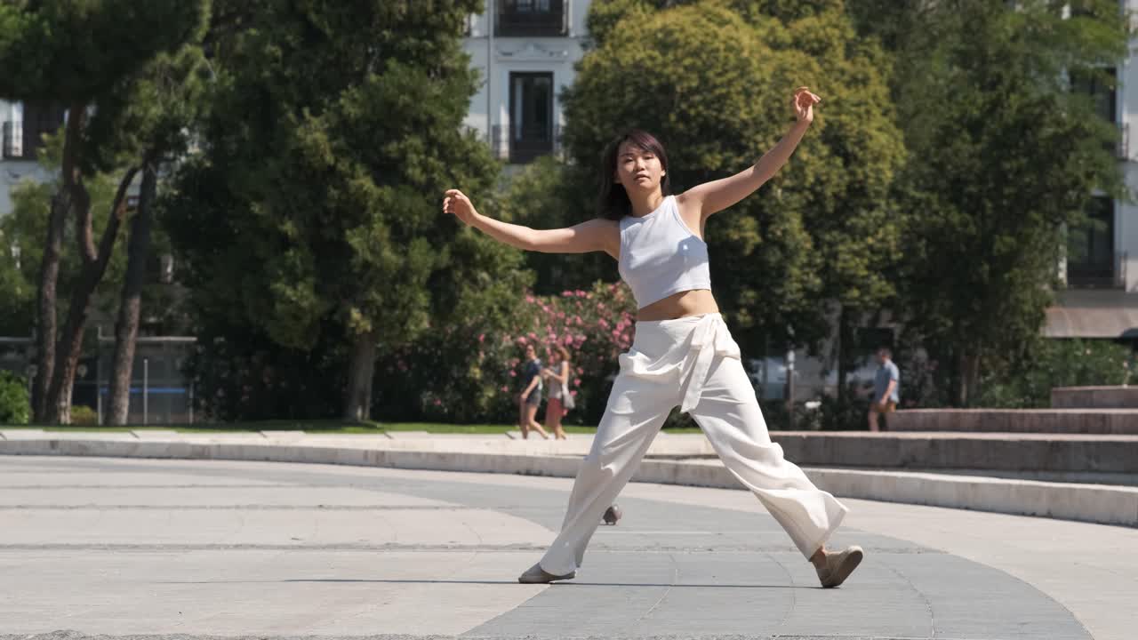 Woman performing freestyle dance on footpath in city park during sunny day