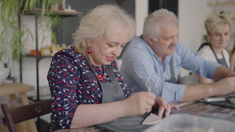 three elderly people work on a potter's wheel in slow motion