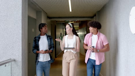 walking in school hallway, students discussing while holding tablet and drink