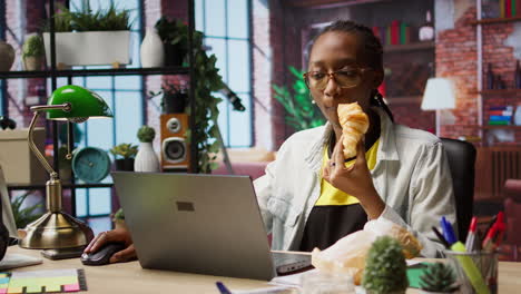 busy freelancer in home office eating snack on the go while typing on laptop