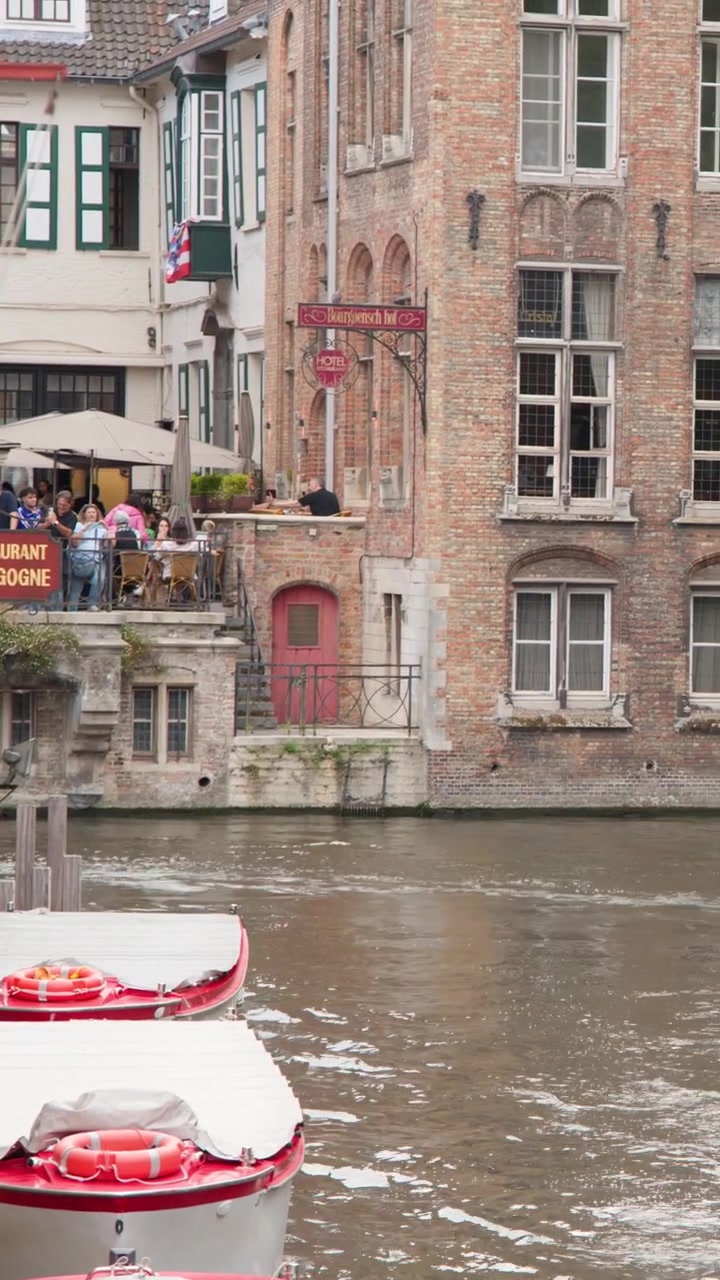 Battello turistico scivola lungo un canale del centro storico, architettura in mattoni, terrazza di un ristorante e acqua riflettente