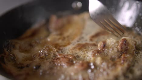 someone stirs pieces of meat on a skillet with a fork