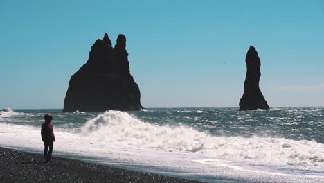 Silueta-Frente-Al-Océano-Mientras-Grandes-Olas-En-Cámara-Lenta-Golpean-La-Playa-De-Arena-Negra-En-Reynisfjara