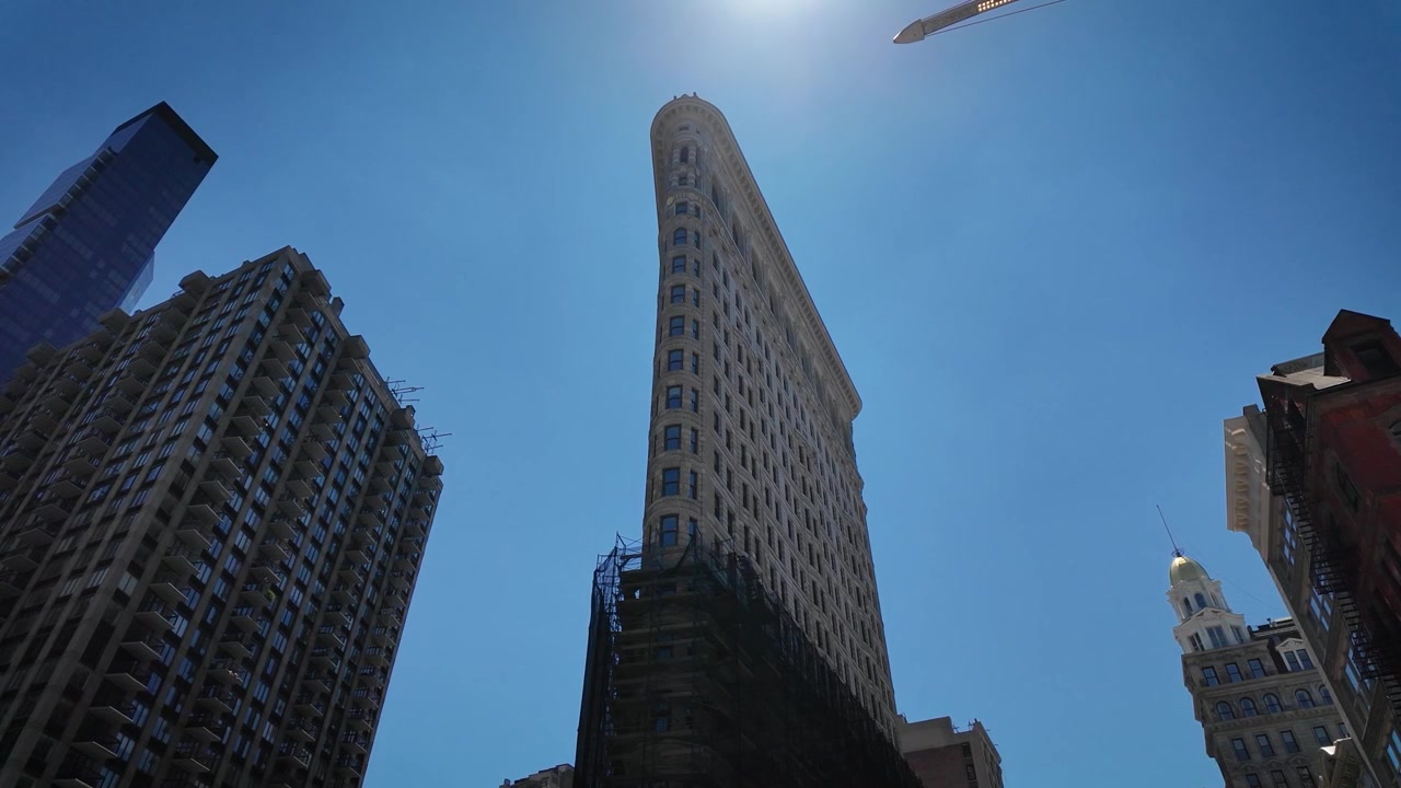 Vista dal basso dell'iconico Flatiron Building che si erge in un cielo estivo di un blu intenso a Manhattan, New York City. Architettura classica Beaux-Arts incorniciata dai grattacieli circostanti