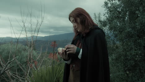 una mujer misteriosa lee un libro esotérico en las montañas entre los árboles.