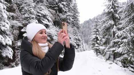 blonde girl holds a smartphone in her hands and takes pictures of a beautiful winter forest blonde girl holds a smartphone in her hands and takes pictures of a beautiful winter forest nature photos for social networks travel and tourism concept