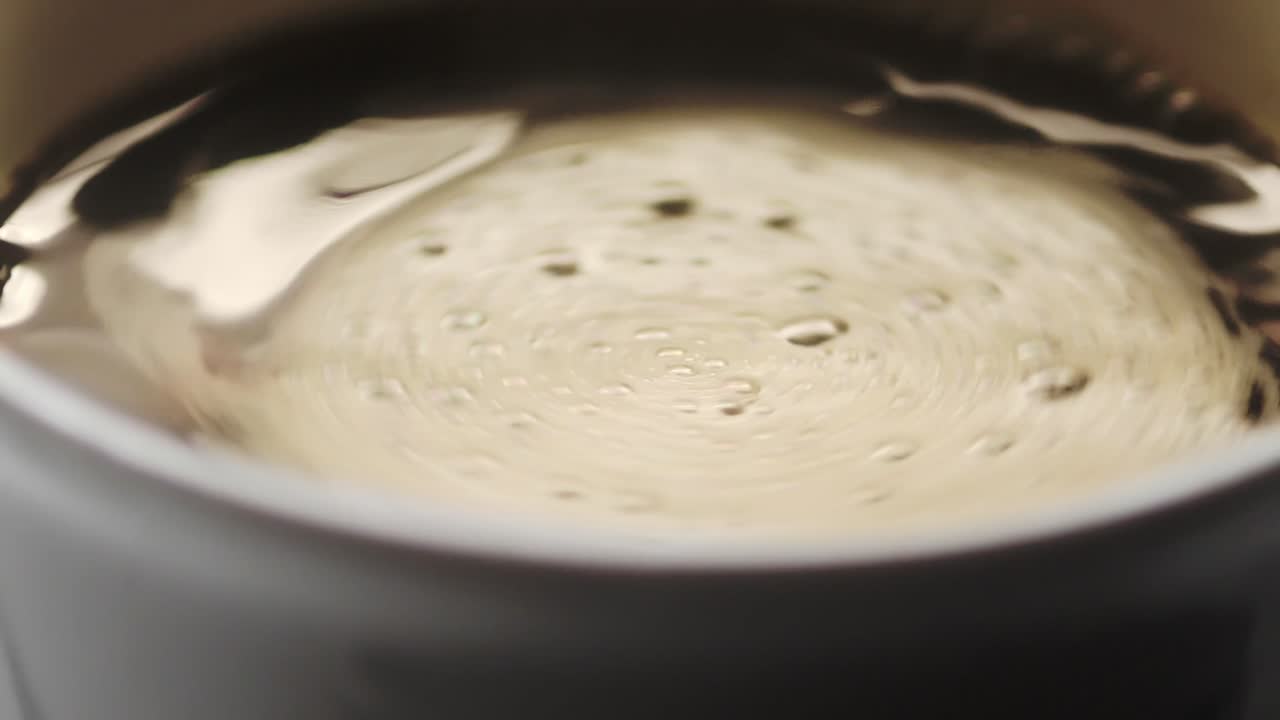 Slow motion top view of a cup filled with coffee, creating a swirl after stirring with a spoon