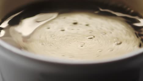 slow motion top view of a cup filled with coffee, creating a swirl after stirring with a spoon